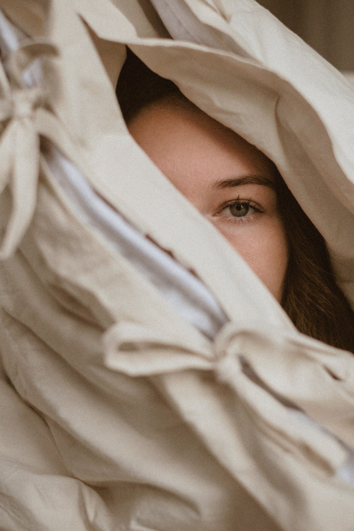 A woman wrapped in an UNWONTED alpaca duvet in a natural-coloured cover, from our collaboration with TAMEKO